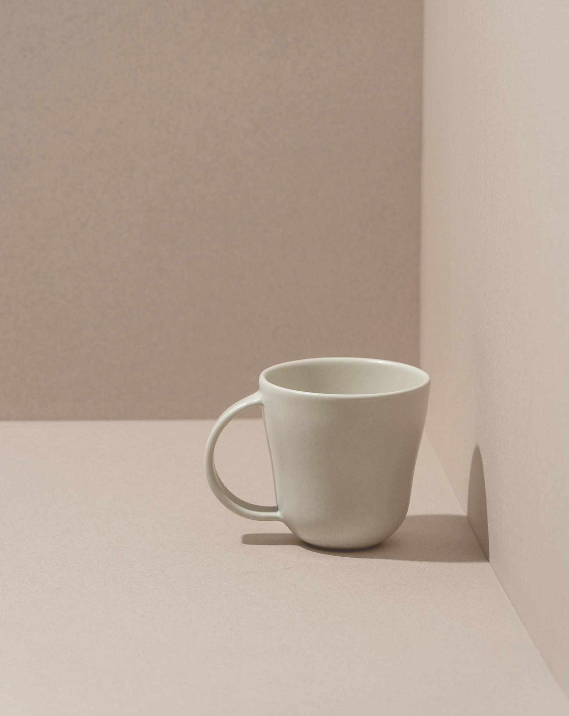 A white stoneware coffee mug placed against a neutral background.