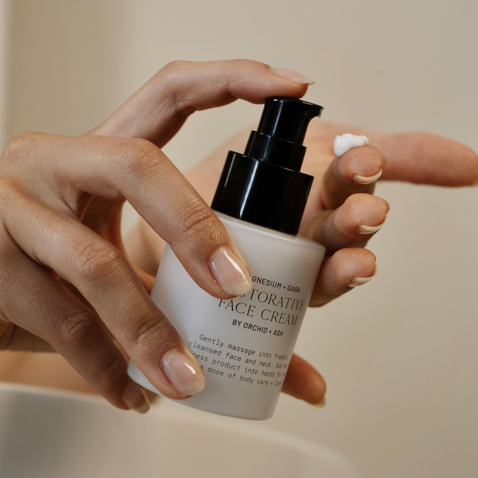 Hand holding a bottle of face cream with a neutral background