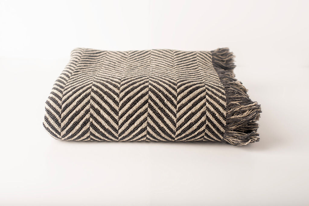 Front view of folded charcoal and cream herringbone woven cotton throw on a white background