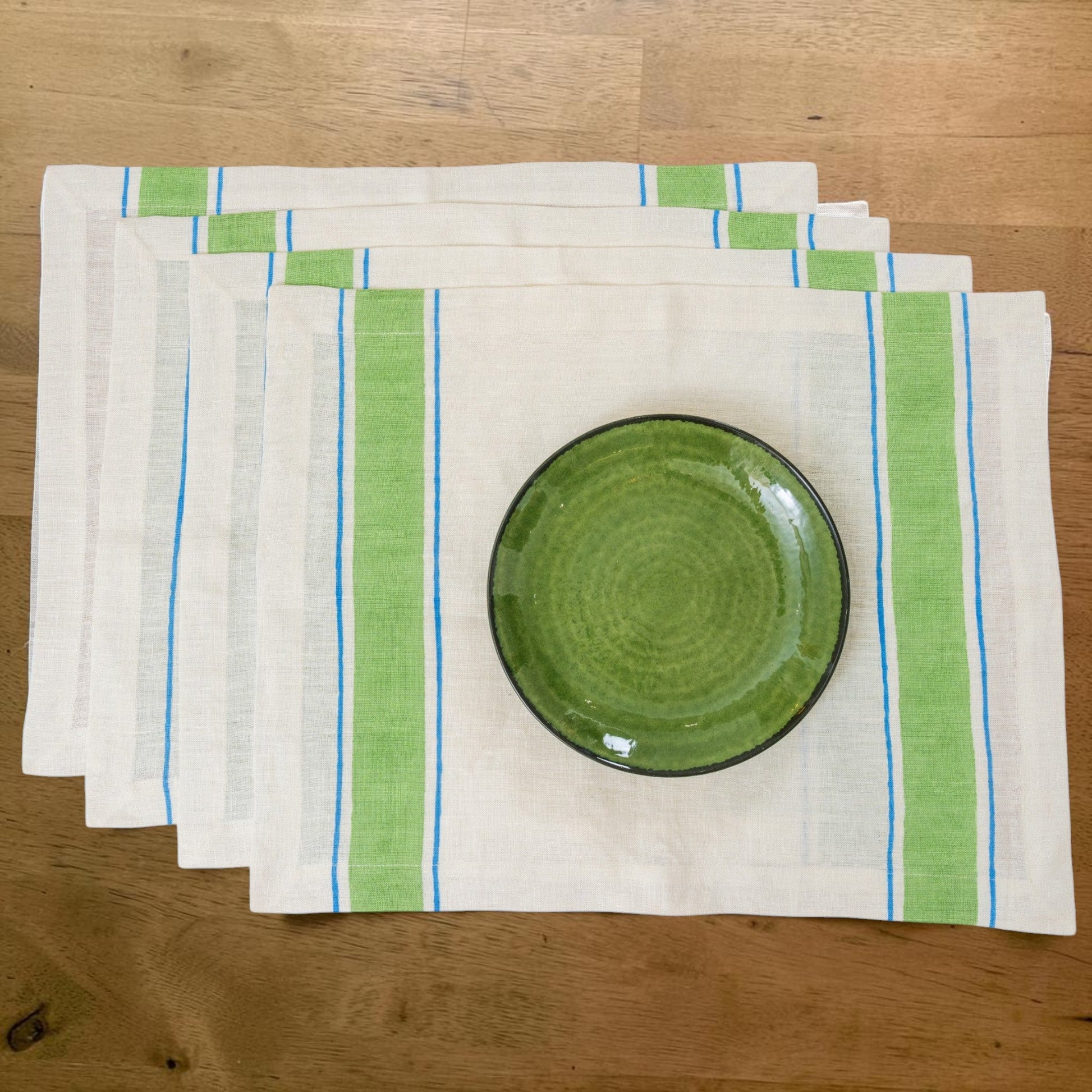 Set of green and blue striped hand block printed linen placemats with a green ceramic plate on a wooden surface