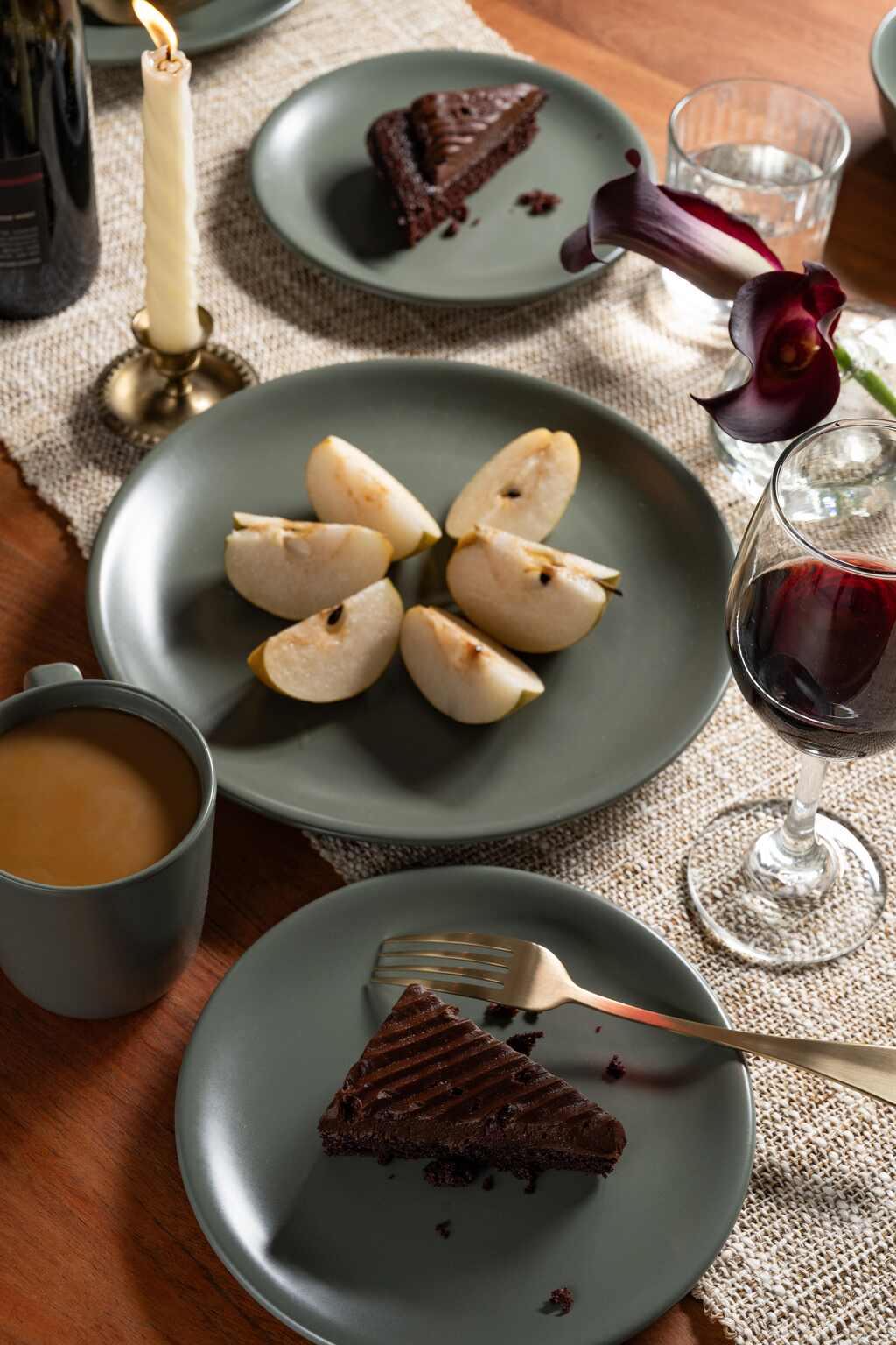 Moss green colored ceramic dinner plates from Hamkke Home styled with sliced pears, chocolate cake, red wine, and coffee on a warm, candlelit tablescape.