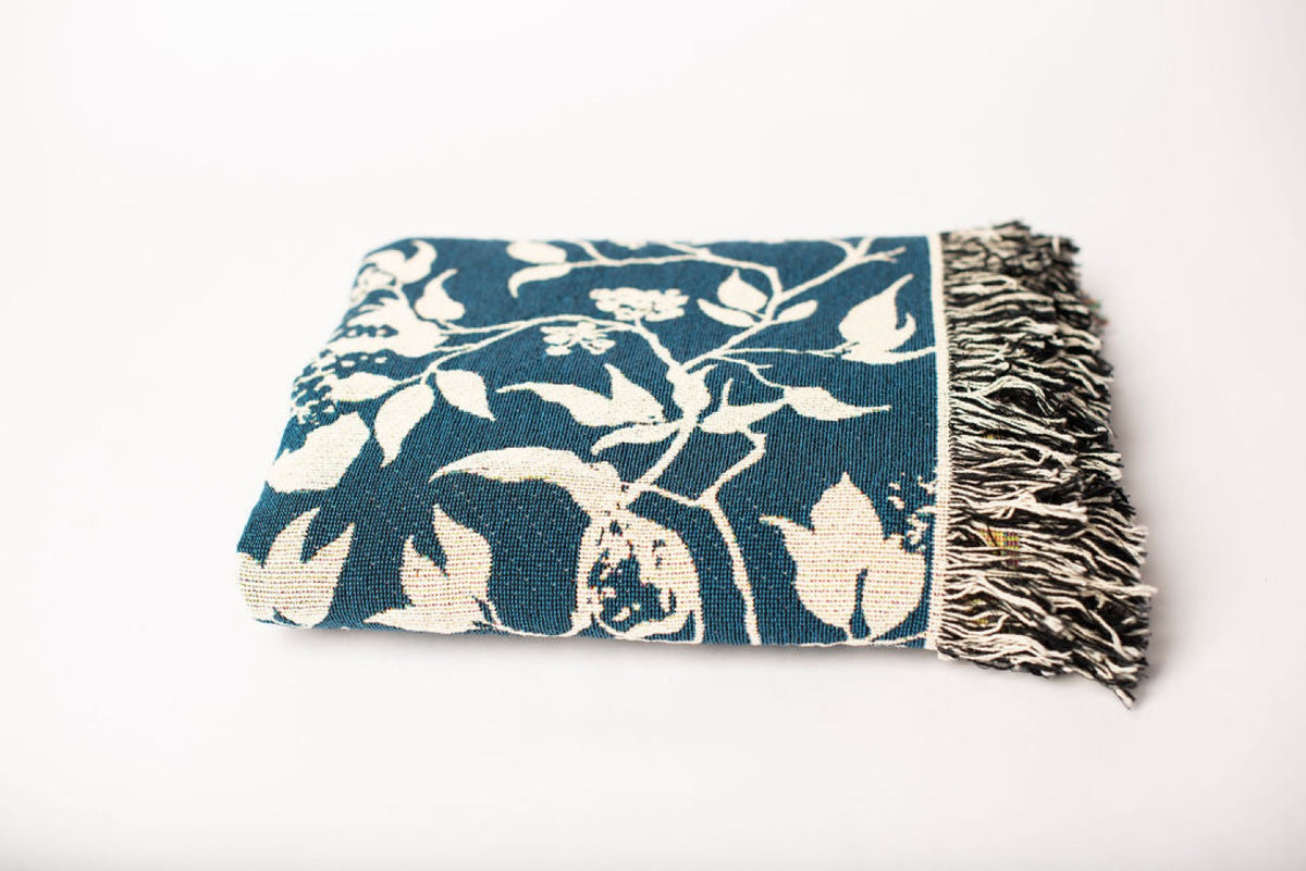 Close-up of Wren Tidesong teal and cream bird and botanical jacquard woven cotton blanket with fringe
