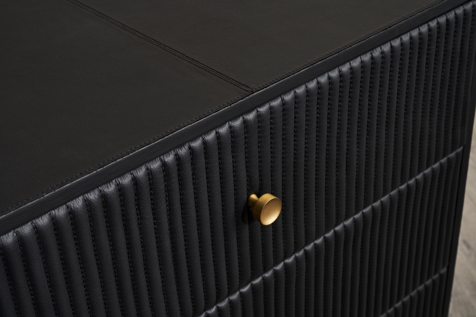 FN-5202-262028_8|Close-up of black leather nightstand drawer front, intricate vertical stitching texture, and elegant round gold knob. High-quality furniture.