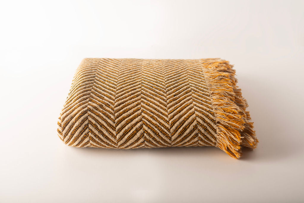 Folded gold and neutral chevron-patterned blanket on a white background