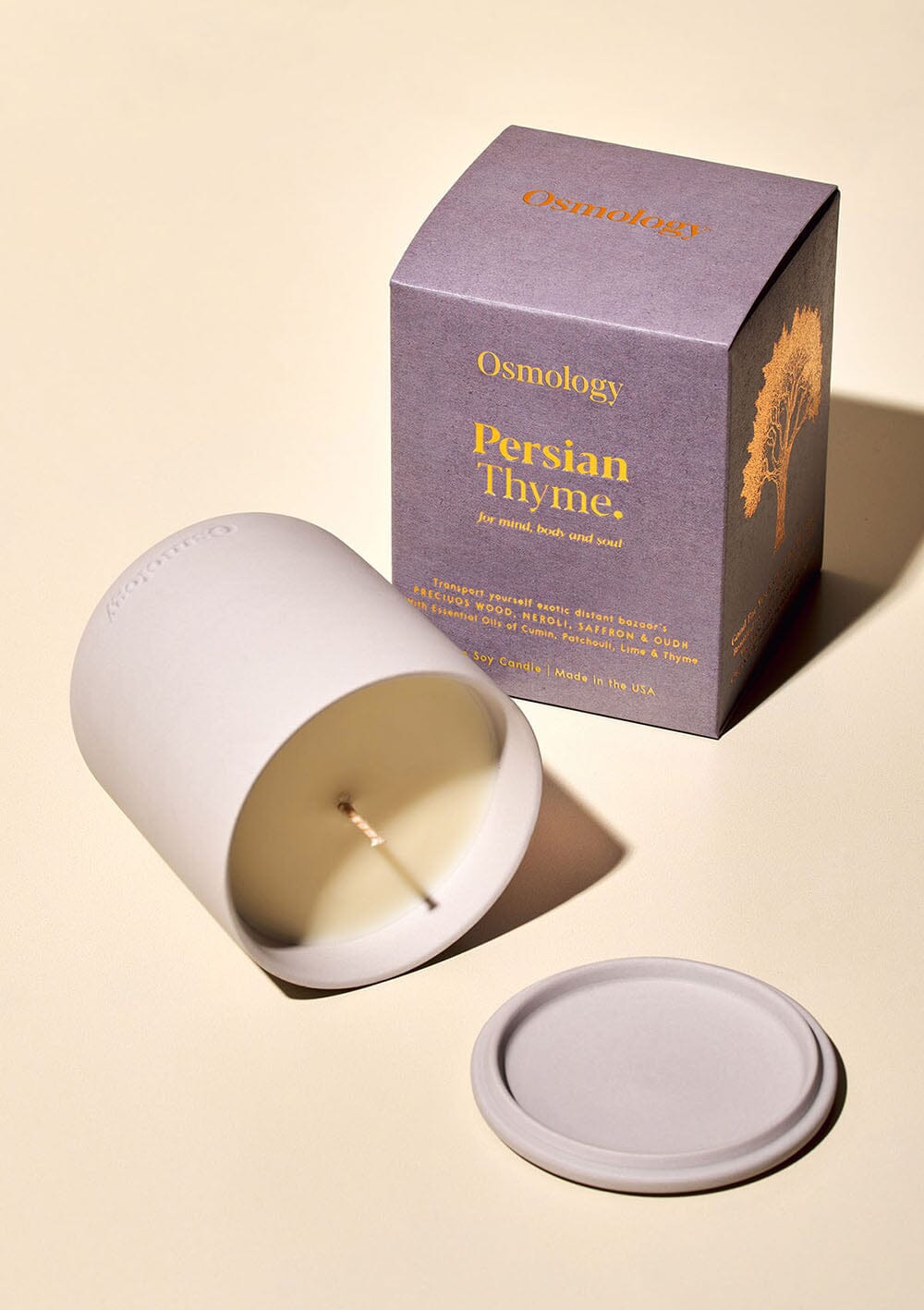 Osmology persian thyme scented candle displayed on it's side next to matching lid and product packaging