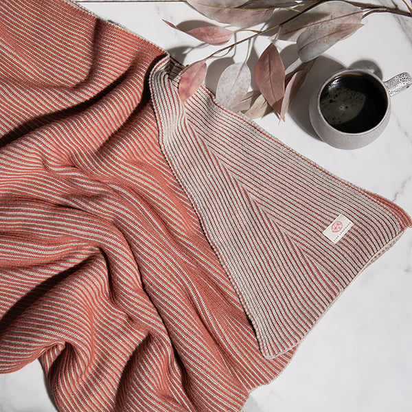 Rust and grey coloured ribbed throw blanket with a cup of coffee and decorative plants. 