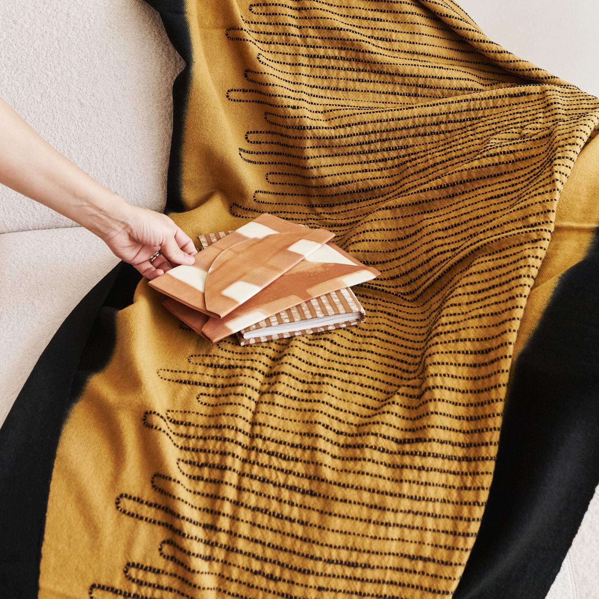 Handwoven Topaz Brown Myrtle Drift Merino Throw displayed on a couch with patterned cushions.