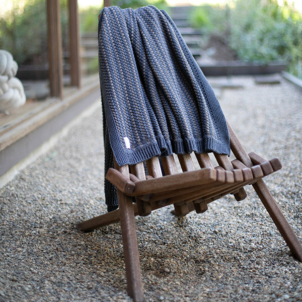 Wooden folding chair placed in an outdoor setting on gravel sand with a blue cotton blanket draped over it.