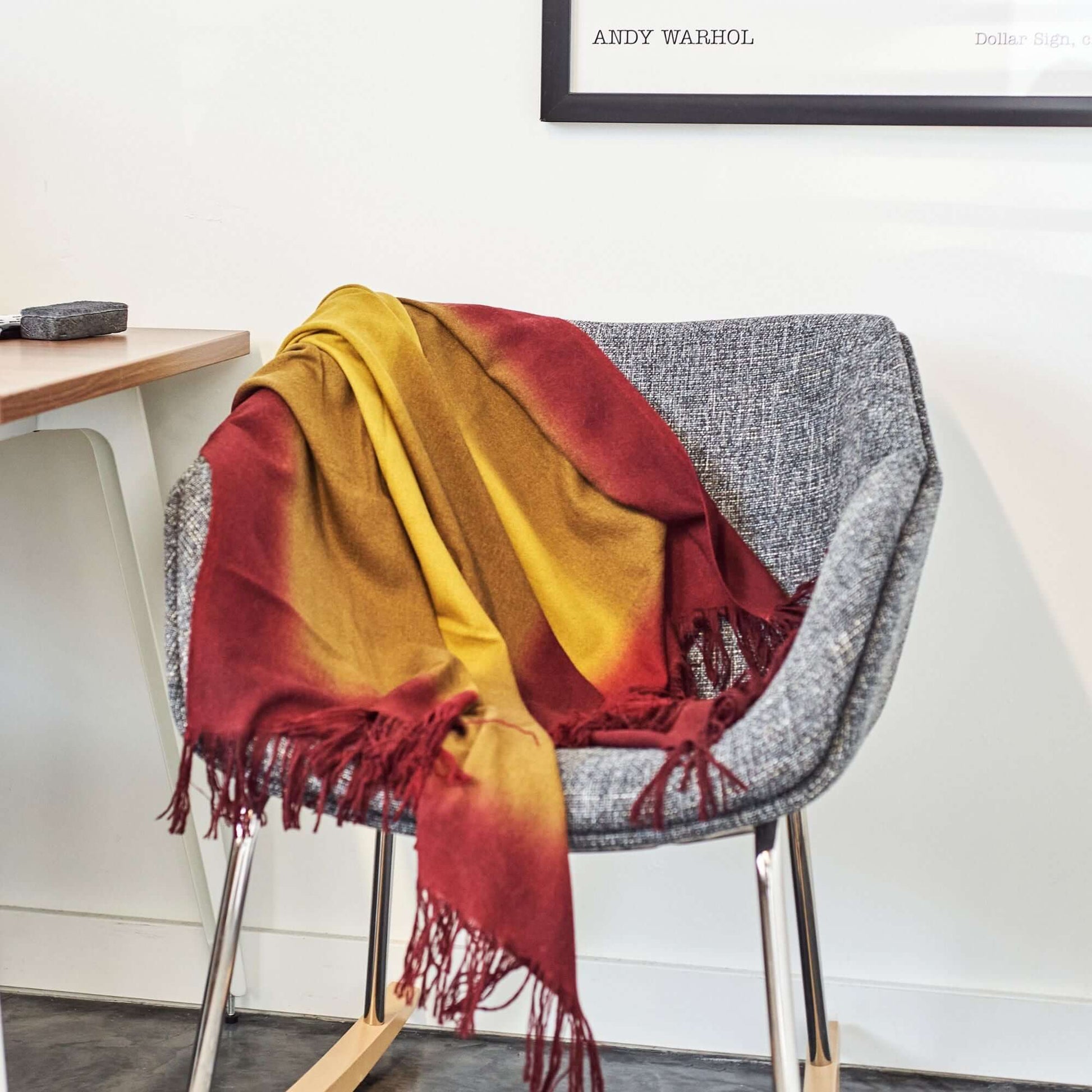 Marigold Merino Ombre Handloom Throw / Blanket Scarf draped over a modern chair, showcasing warm gradient colors and fringe detailing.