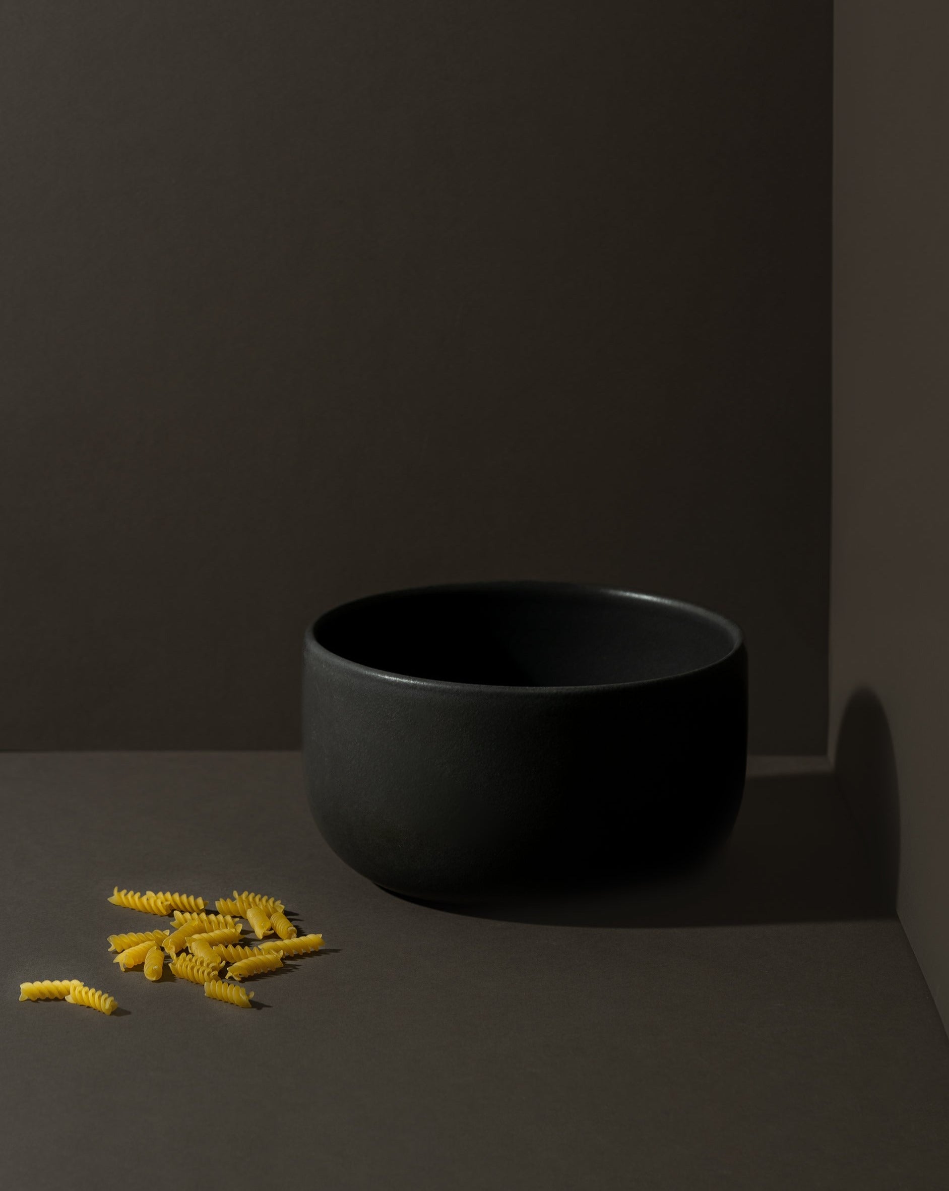 Matte black stoneware bowl with a few pieces of pasta placed beside it.
