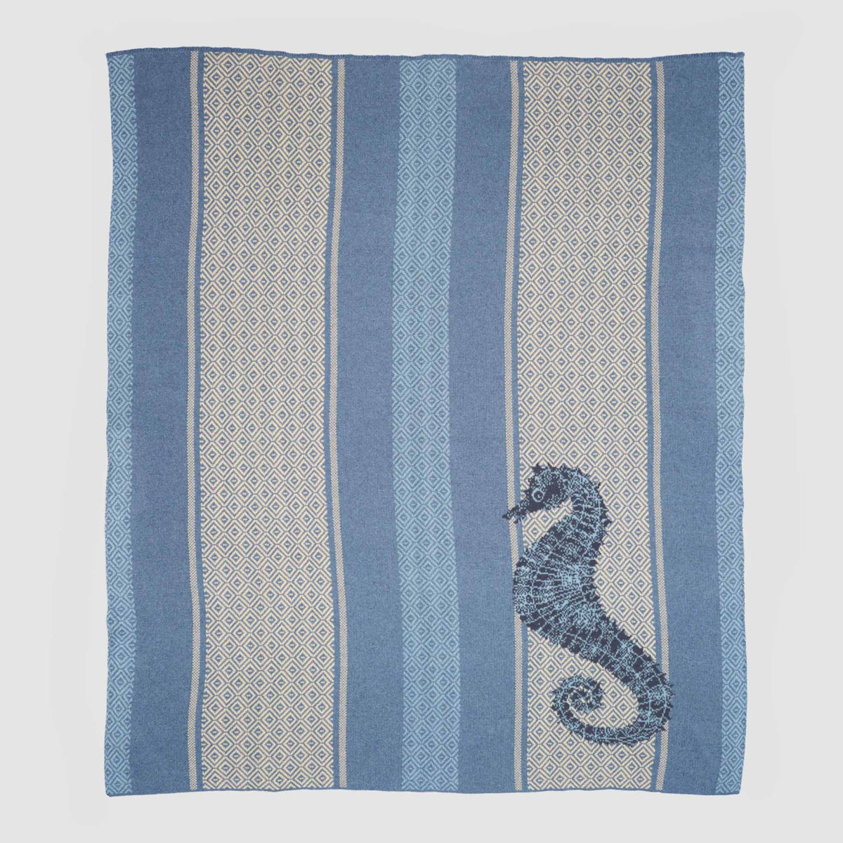 The Seahorse Square - Cotton Sustainable Knit Throw Blanket from In2Green features a blue and cream woven design with geometric stripes and a dark blue seahorse motif in one corner, displayed flat on a white background. Crafted from soft recycled cotton, this coastal knit throw adds a nautical touch to your decor.
