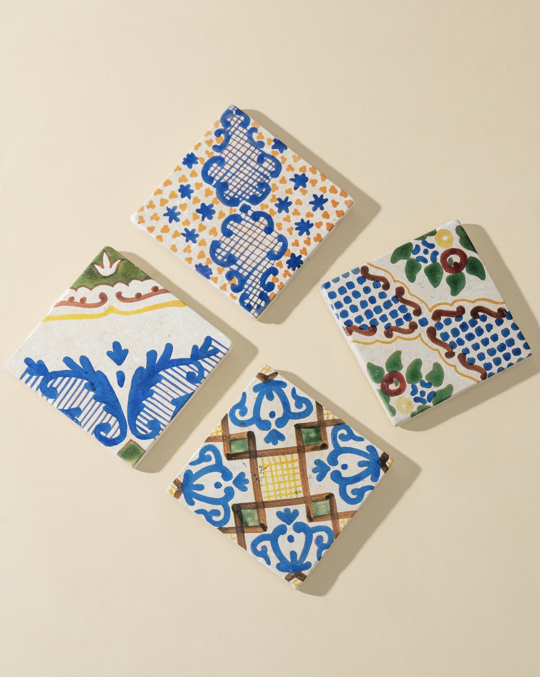 A set of four square marble coasters with hand-finished white and blue patterns, displayed on a neutral background.