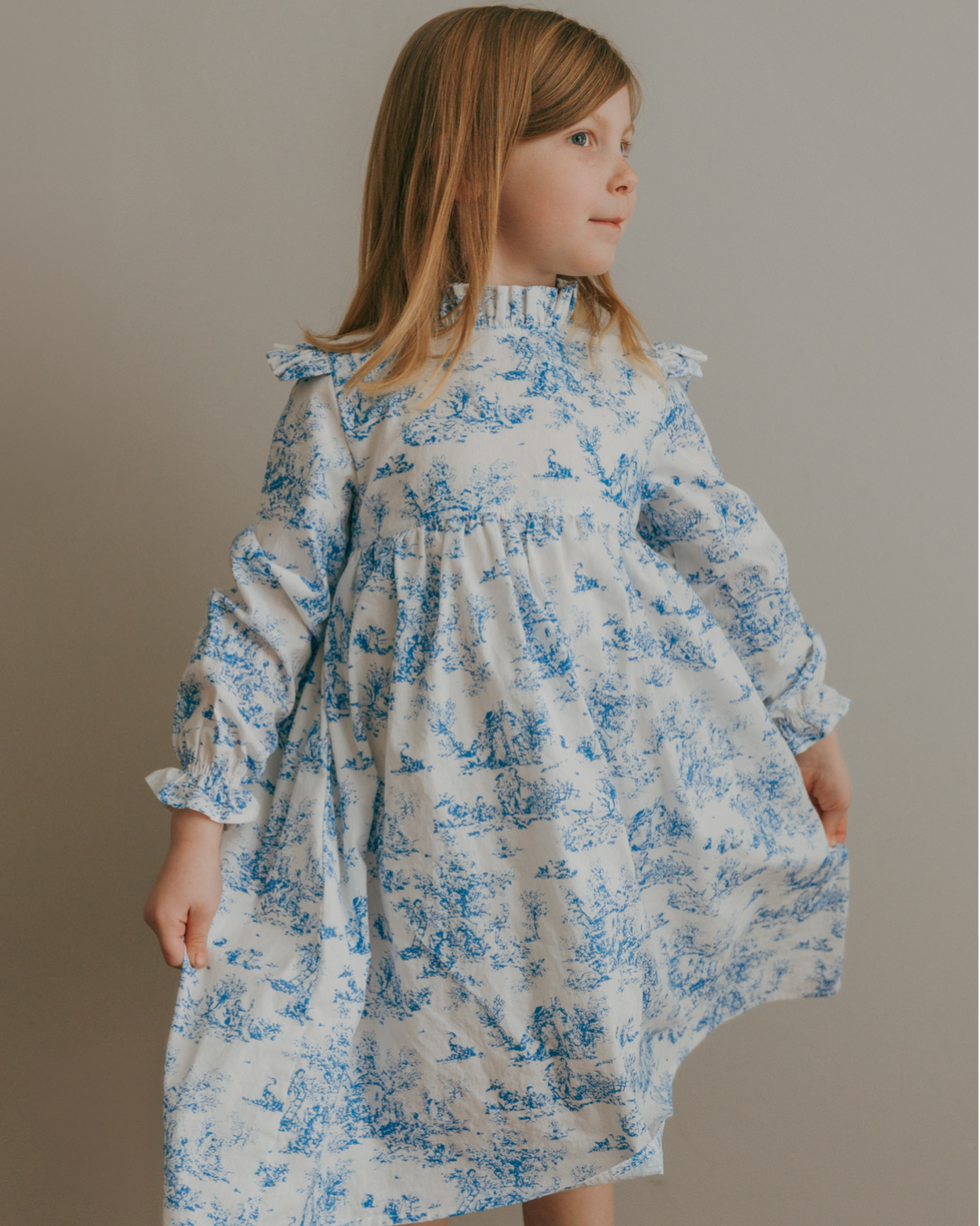 Child wearing a blue toile floral dress against a plain background