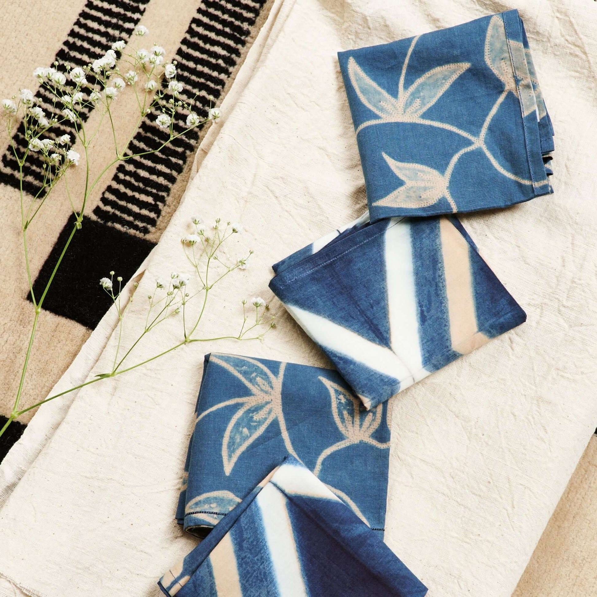 Tisa Indigo Hand Crafted Shibori Print Cotton Table Napkin set of 4 displayed with flowers on a light cloth background.
