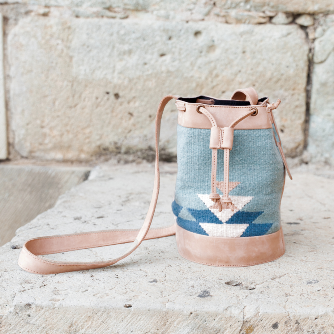 Handwoven blue wool and leather cinched bucket bag with adjustable strap, featuring a soft silhouette inspired by river currents; artisan-made and spacious.