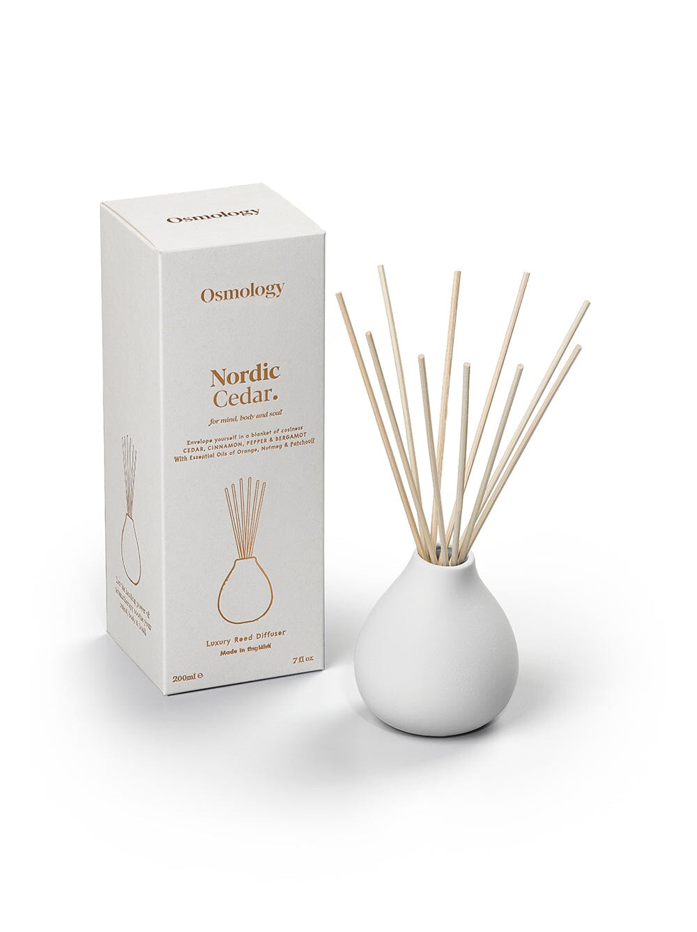 Osmology Nordic cedar ceramic reed diffuser in white next to product packaging on an orange-cream background