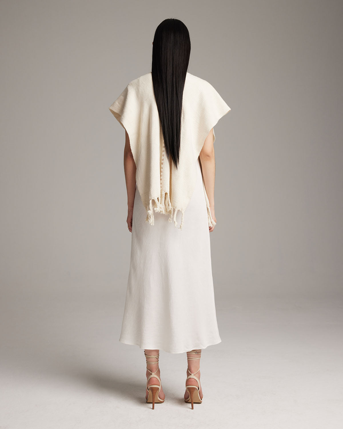 Model wearing a white Copper Threads Manta from the back, showcasing fringe detail.
