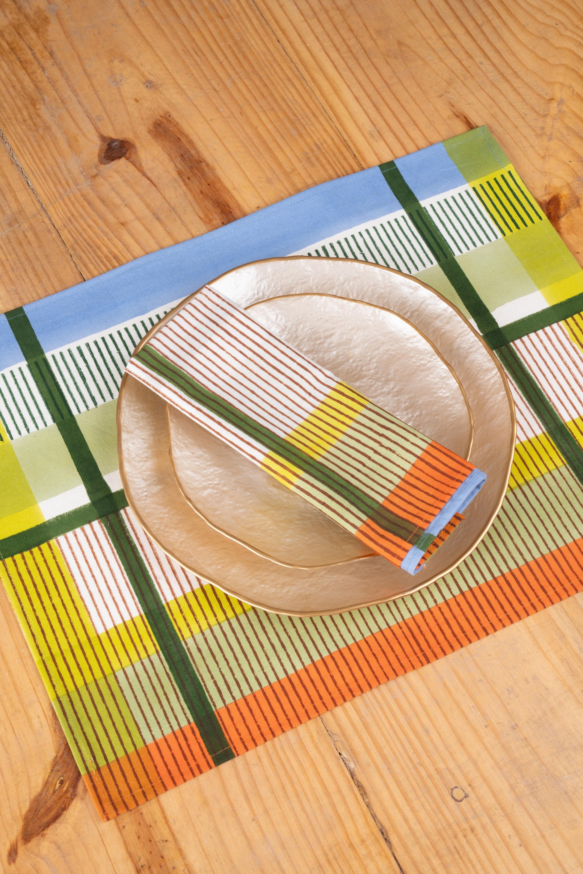 Modernist striped napkin folded beside metallic plates on wooden table