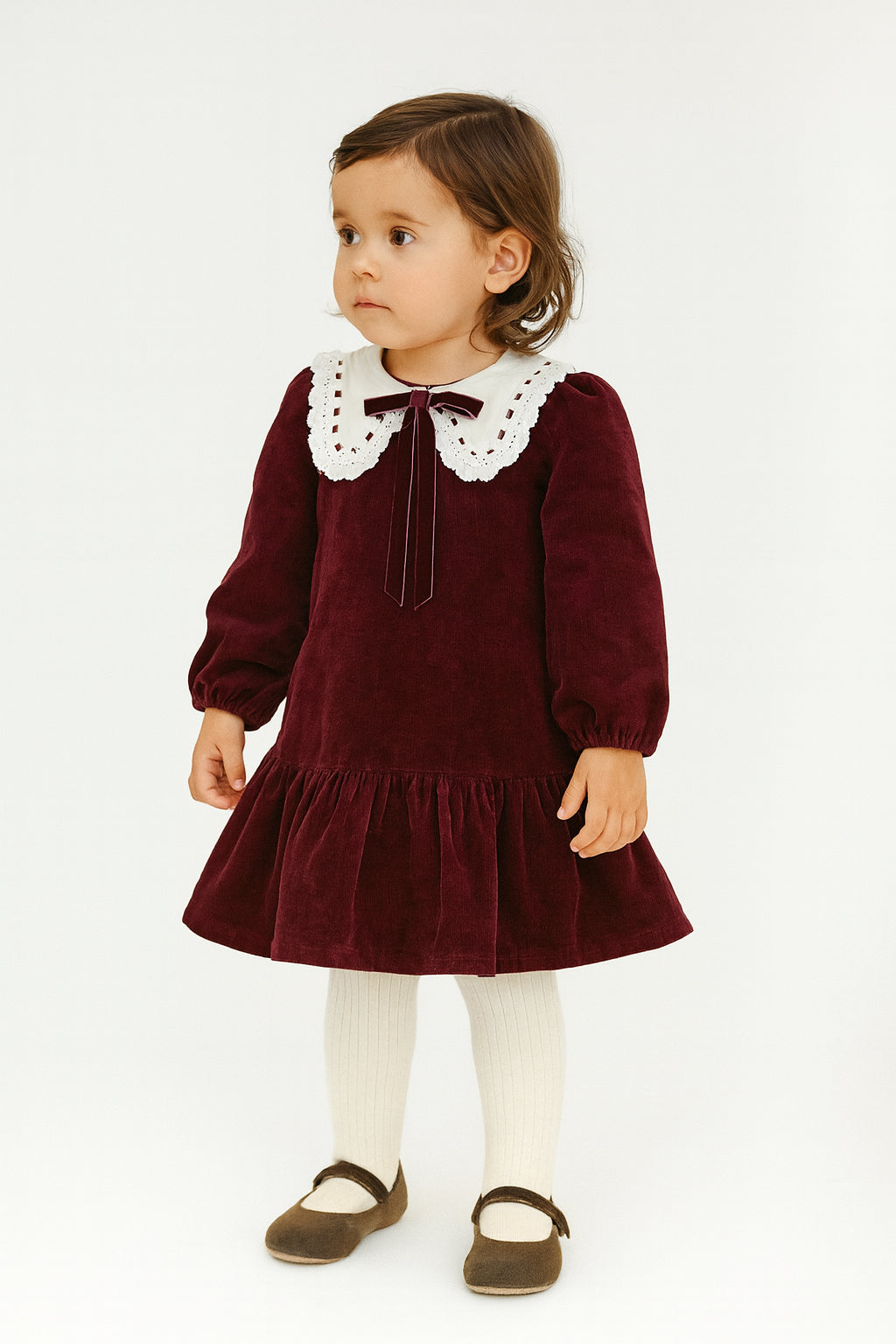 Young girl wearing a burgundy dress with a white collar on a white background