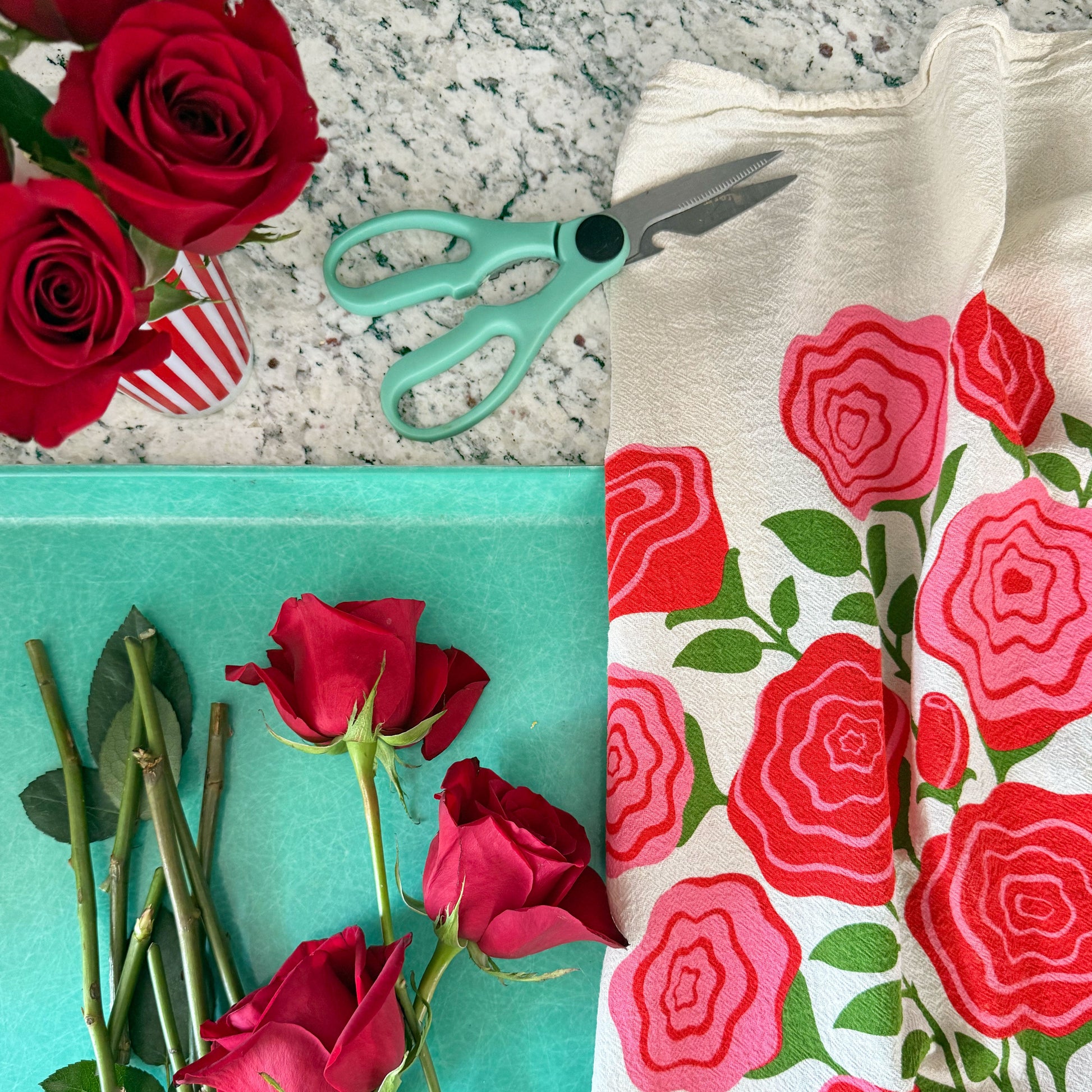 The Neighborgoods Roses dish towel featuring a rose illustration, laid next to freshly cut roses on a kitchen countertop