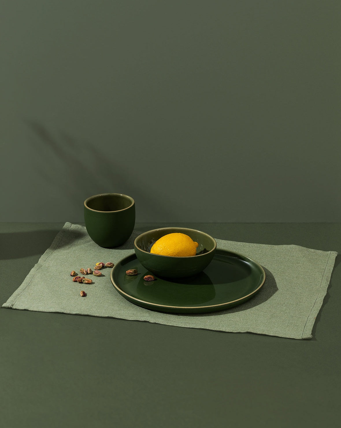 A green cotton placemat on a table with a plate and cup on top, against a dark background.