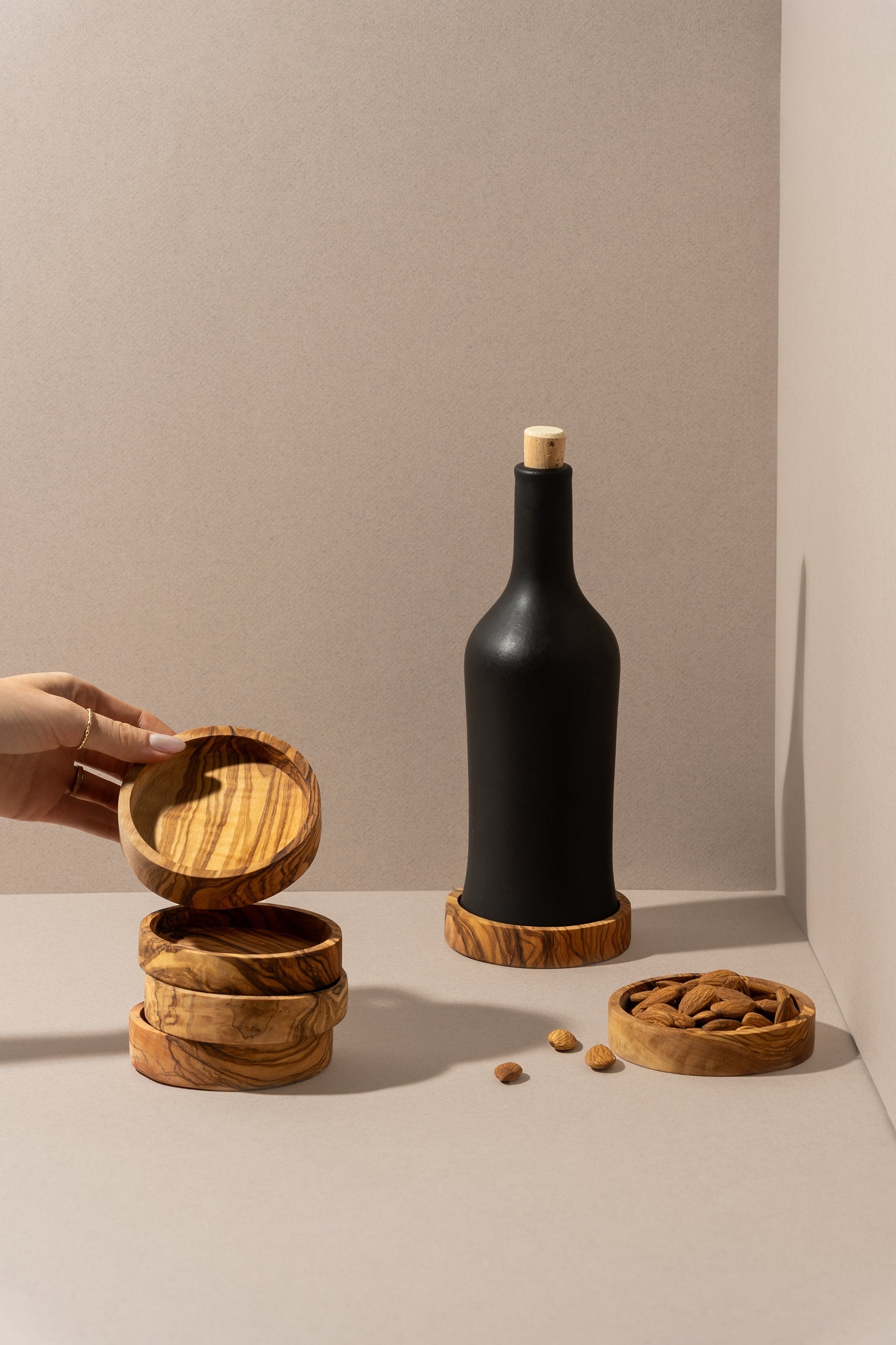 Stacked olive wood bowls, one with a wine bottle and another with walnuts, displayed against a warm background