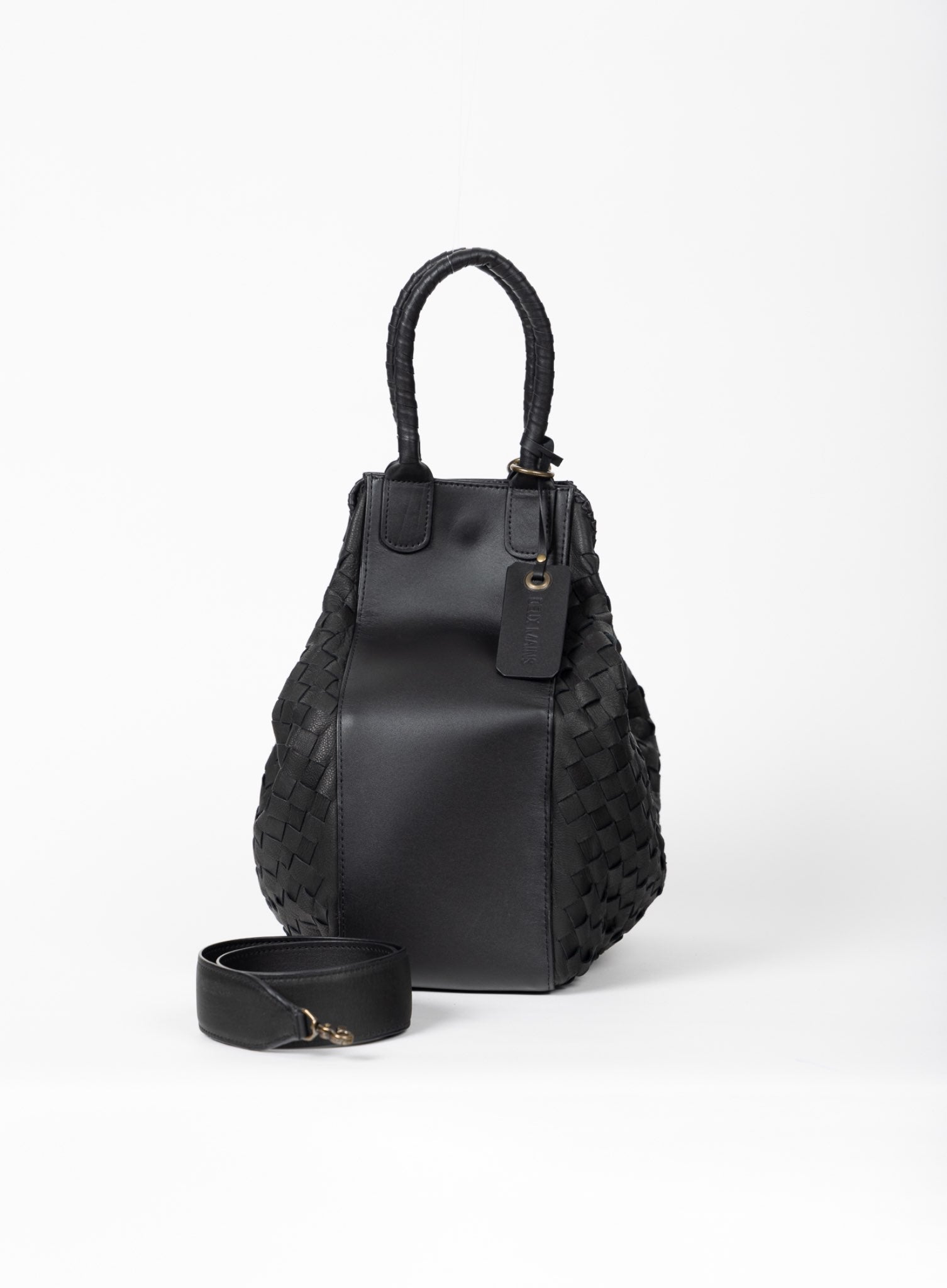 Model standing up holding the all day tote in mahogany and looking at the all day tote in black on the floor with flowers.
