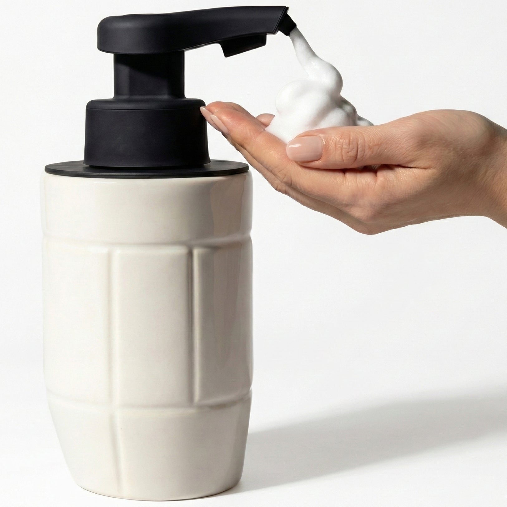 BosilunLife Eco-Brutalism automatic foaming soap dispenser in off-white recycled eco-clay. A person's hand triggers the touchless black sensor pump to dispense rich white foam. The ceramic bottle features a bold, embossed architectural grid pattern, highlighting a modern, hygiene-focused eco-brutalist aesthetic.