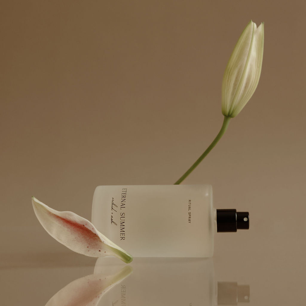 White flower bud and perfume bottle on a reflective surface with a beige background