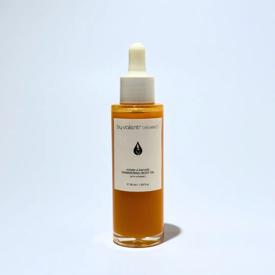 Bottle of By Valenti Organics shimmering body oil with dropper on a light blue background