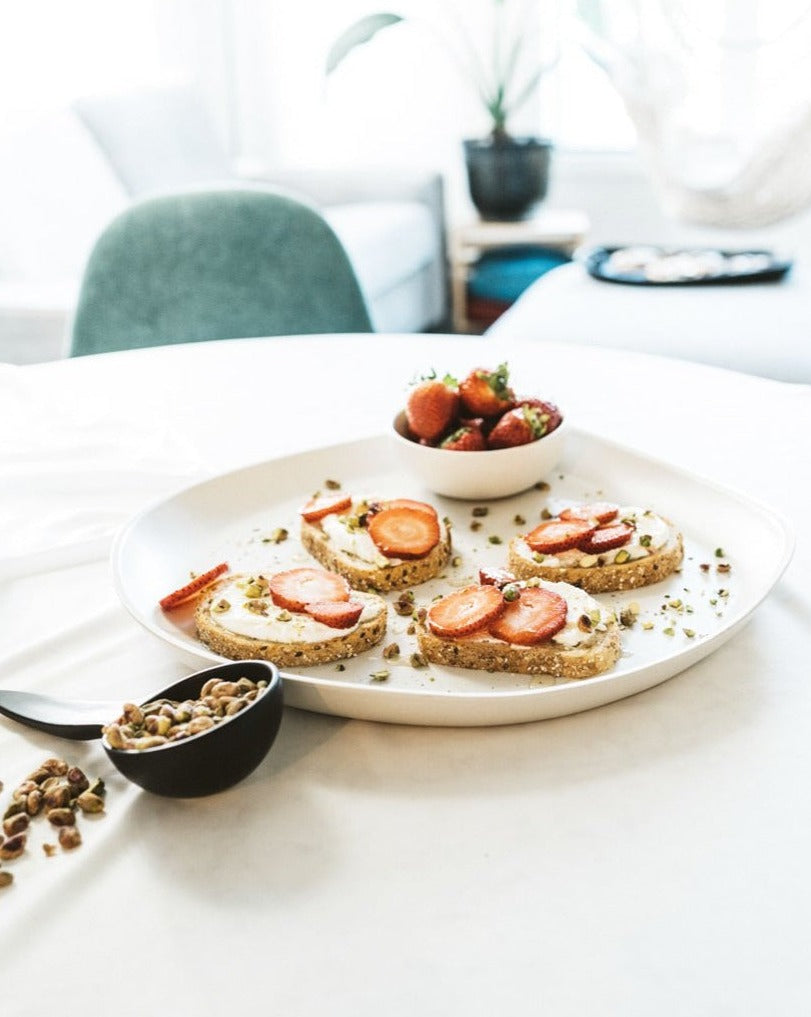 A stoneware serving platter with organic forms and a matte finish, presented on a table with food items arranged on top.