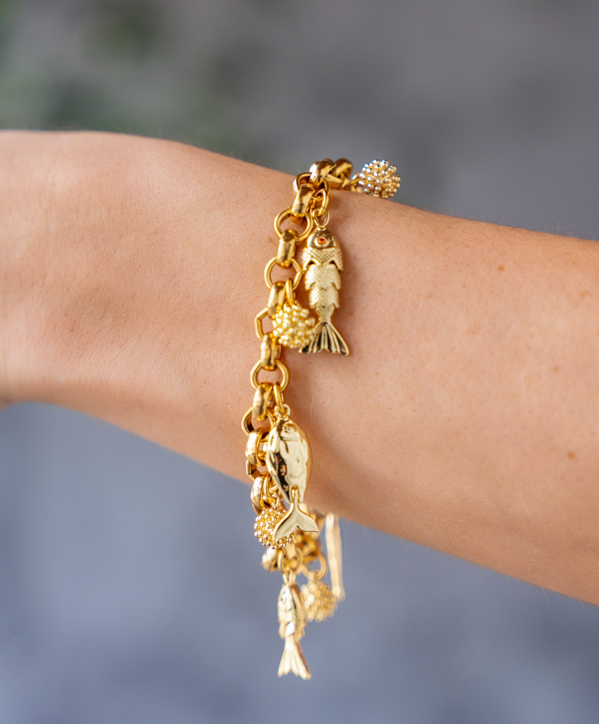 Gold charm bracelet with dangling fish charms and textured gold bead accents on a chunky chain.