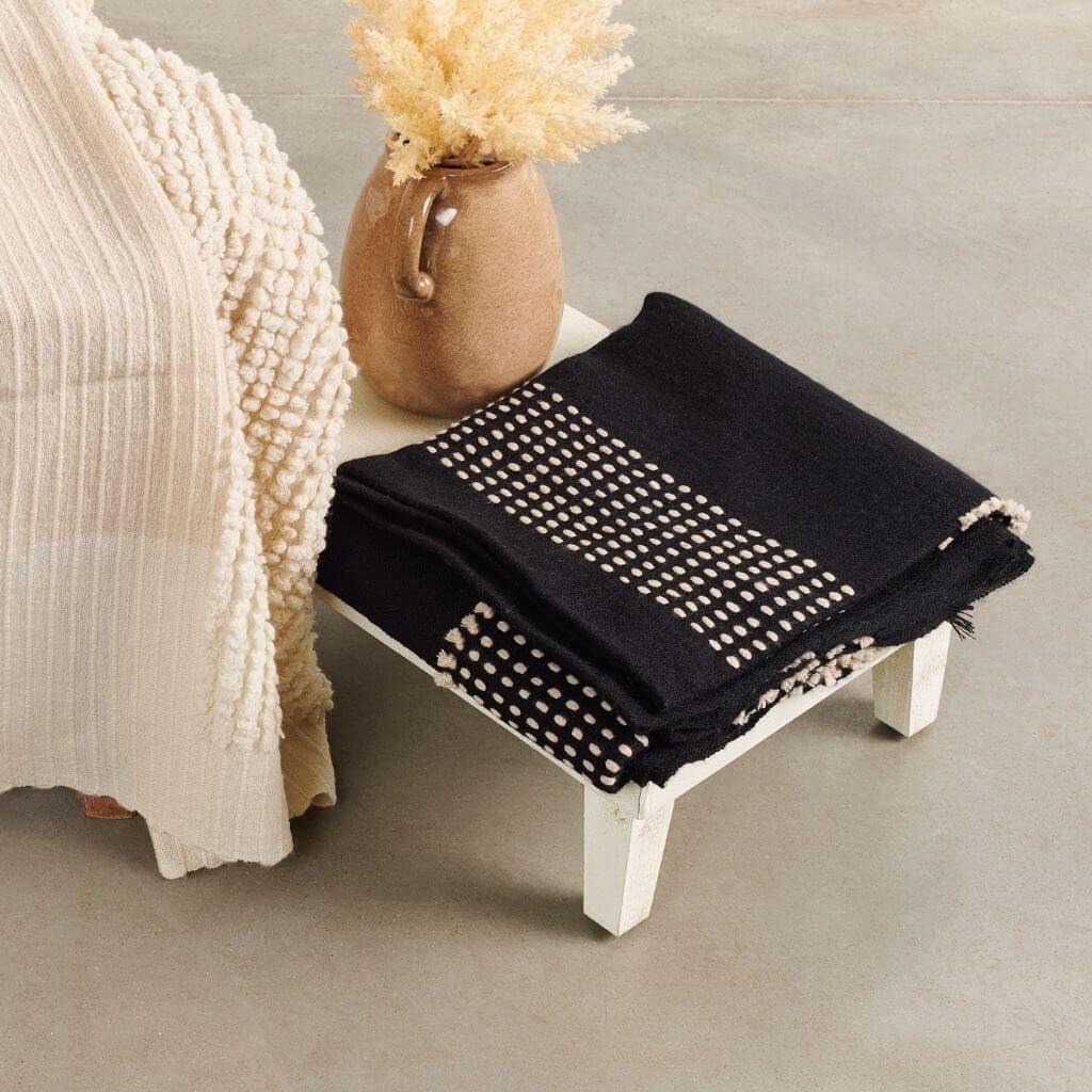 Walnut Black Yak With Hand Knotted Merino Stripes Handloom Throw displayed on a wooden table with a decorative vase.
