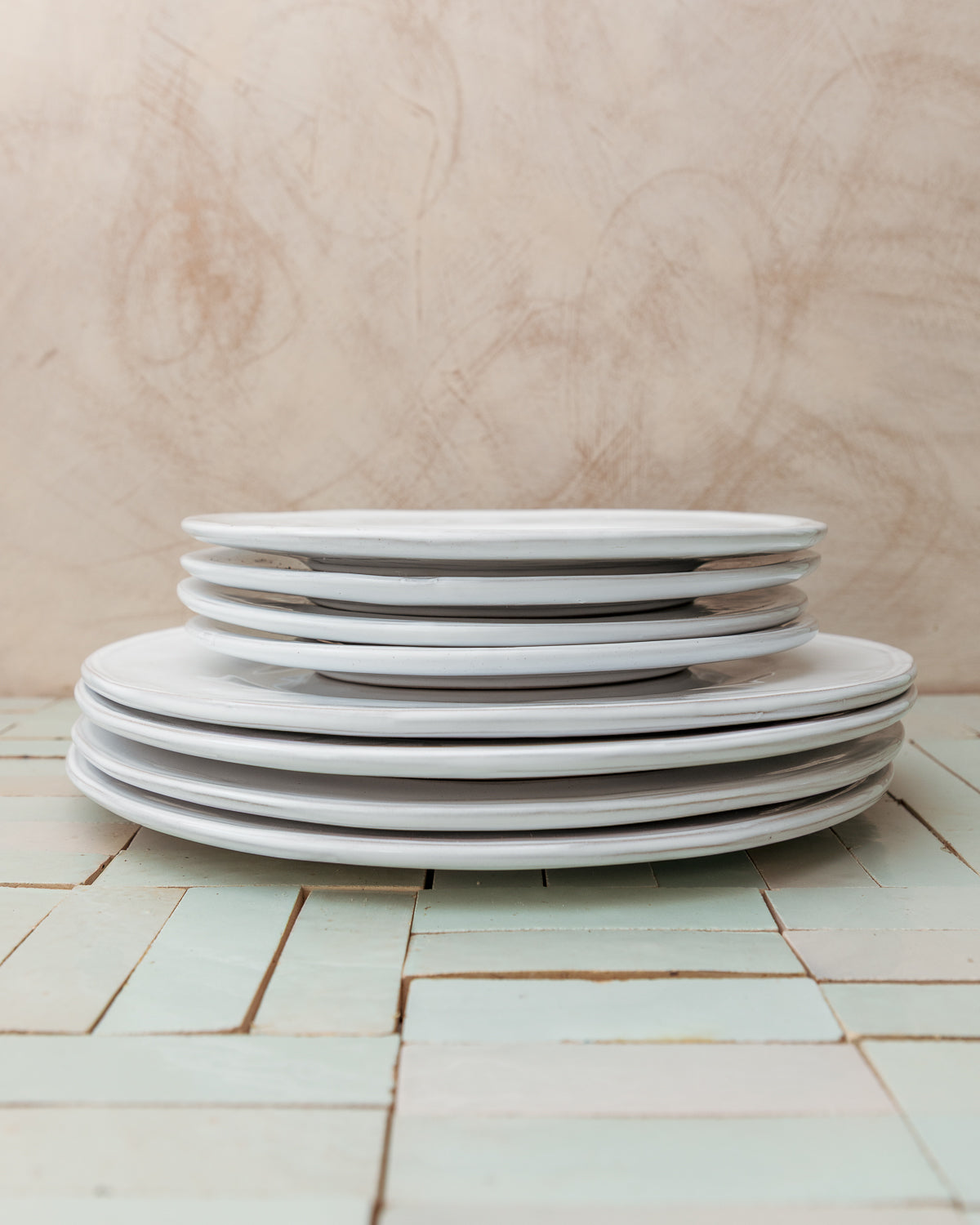 Stack of white ceramic plates on a tiled table with a wooden wall background