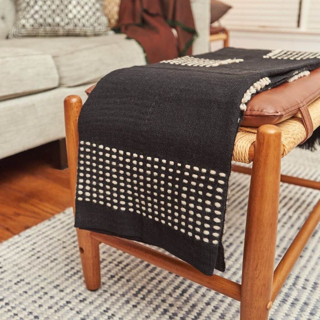 Walnut Black Yak With Hand Knotted Merino Stripes Handloom Throw draped on a wooden chair in a cozy living room setting.