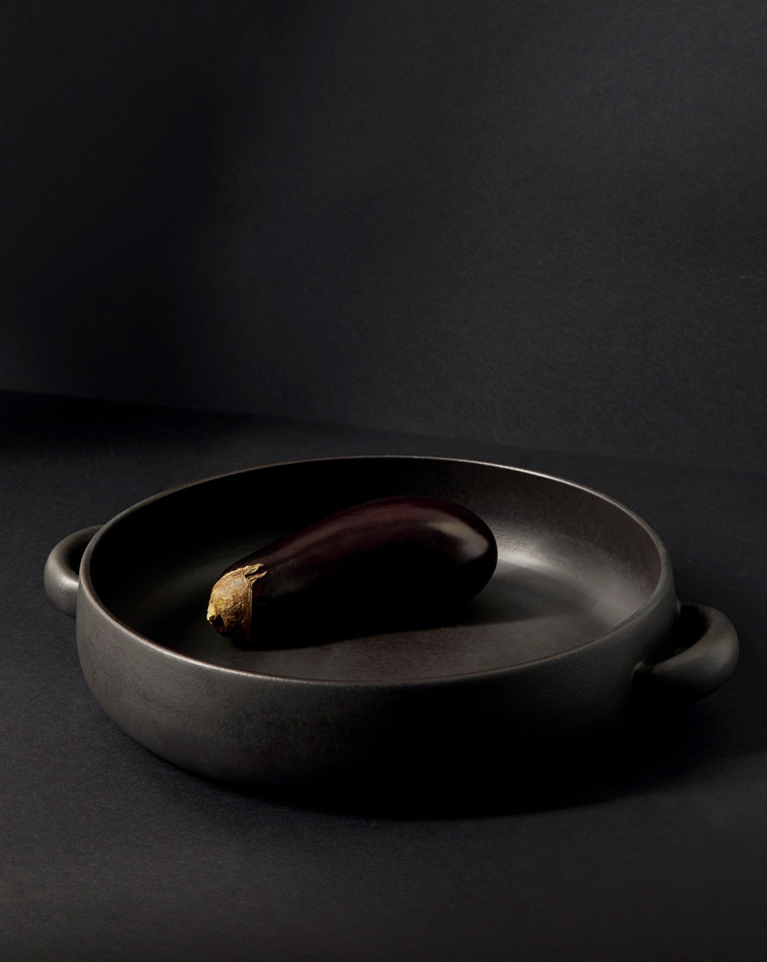 A white stoneware serving plate with handles, featuring a minimalist design, displayed with a piece of cauliflower on it, set against a neutral background.