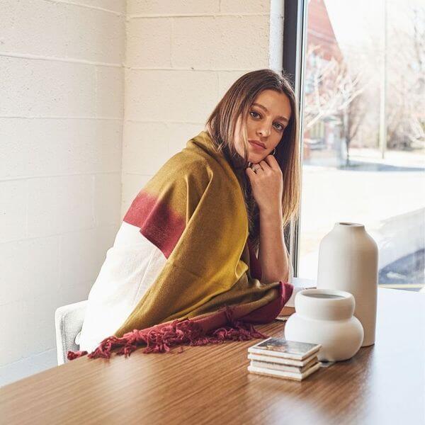 Marigold Merino Ombre Handloom Throw / Blanket Scarf displayed on a woman sitting at a table with decorative items.