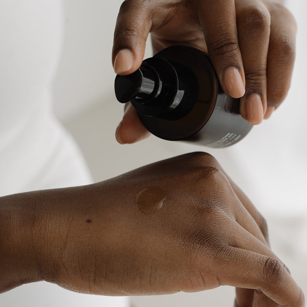 Hand applying a black bottle of skincare product to another hand on a white background