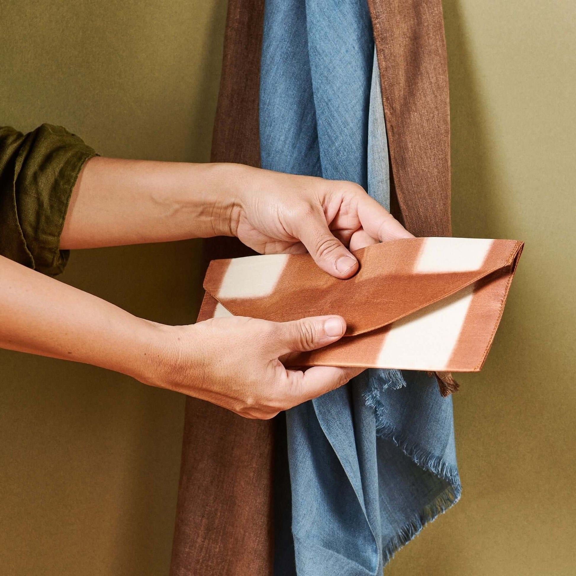Person holding the Melo Gold Mulberry Silk Shibori Hand Crafted Envelope Pouch with a soft fabric backdrop.