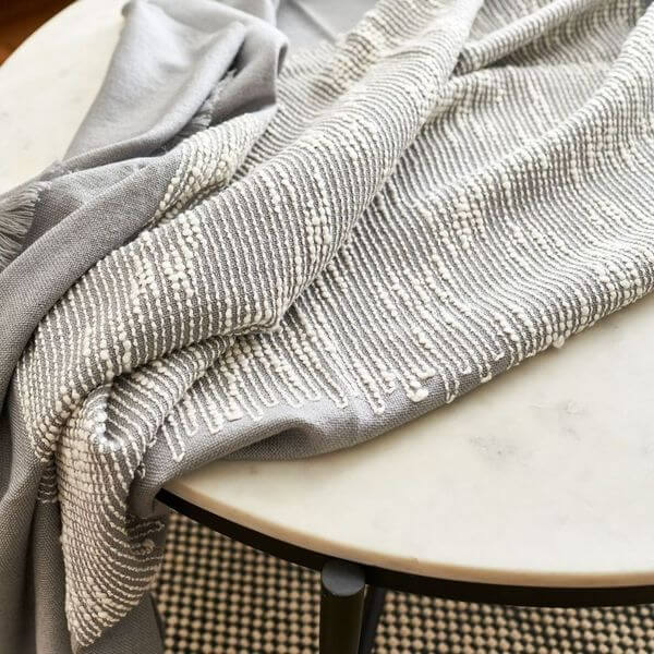 Flo Gray Textured Handloom Merino Throw draped elegantly on a marble table, showcasing its luxurious design and craftsmanship.