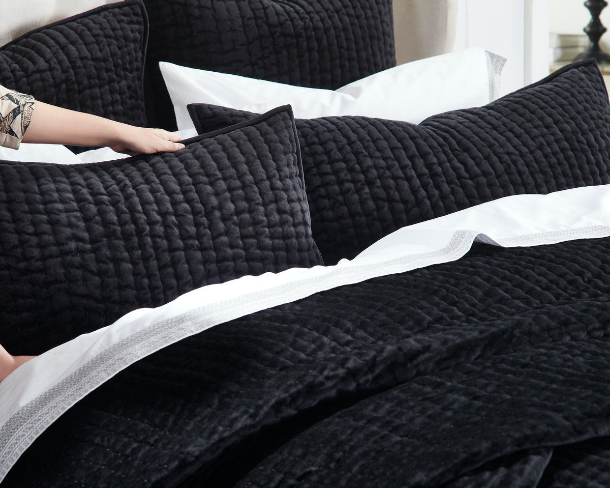 QT-361-9496_4|Hand adjusting a soft black quilted pillow, revealing the cozy textured quilt and crisp white sheets for ultimate comfort.