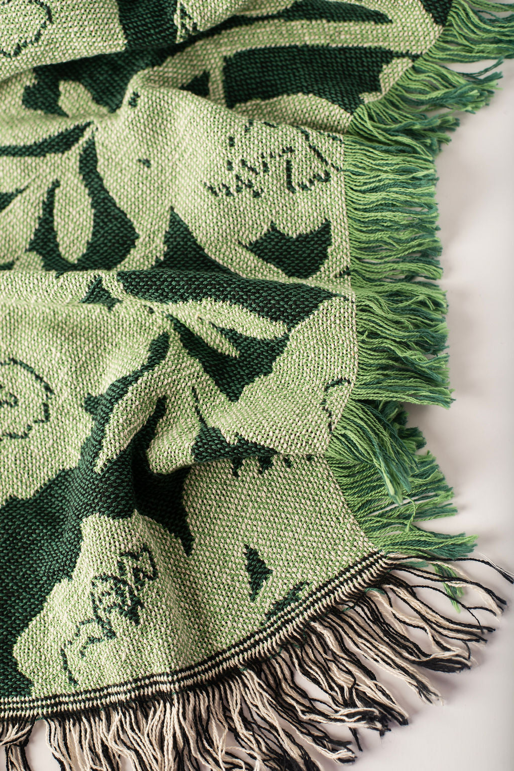 Close-up of Addy Spruce dark and light green floral woven cotton throw with green fringe