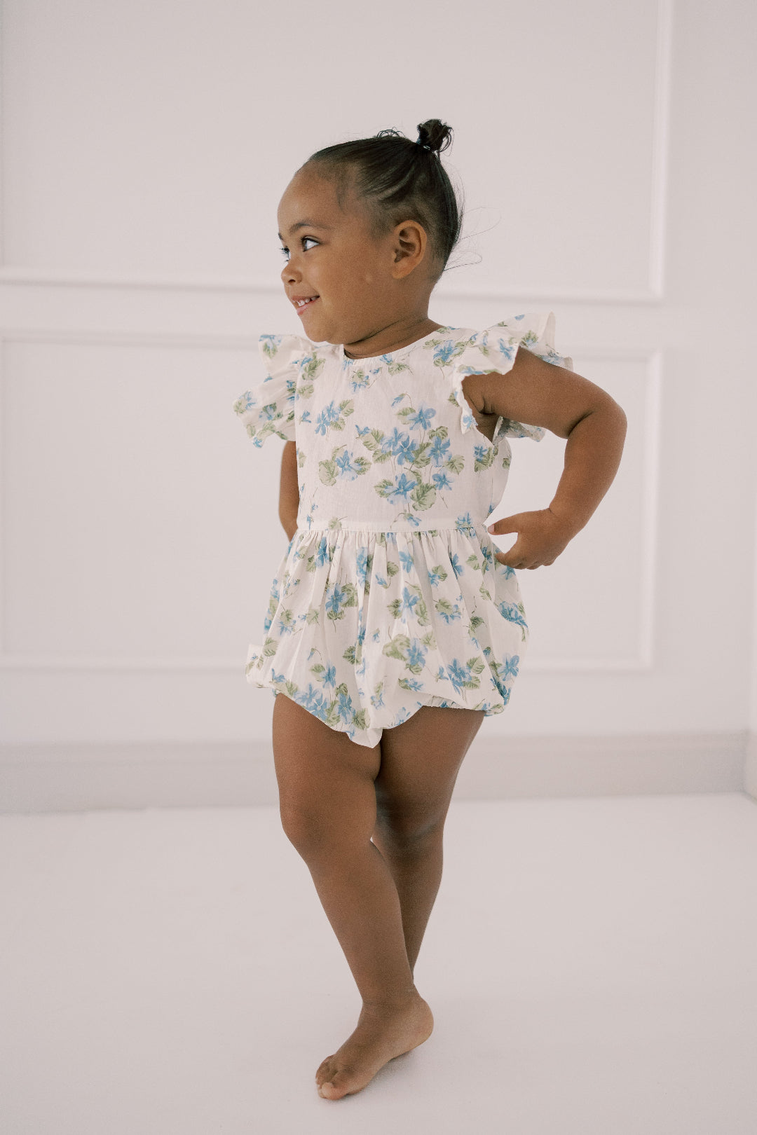 Young girl wearing a floral romper against a white background