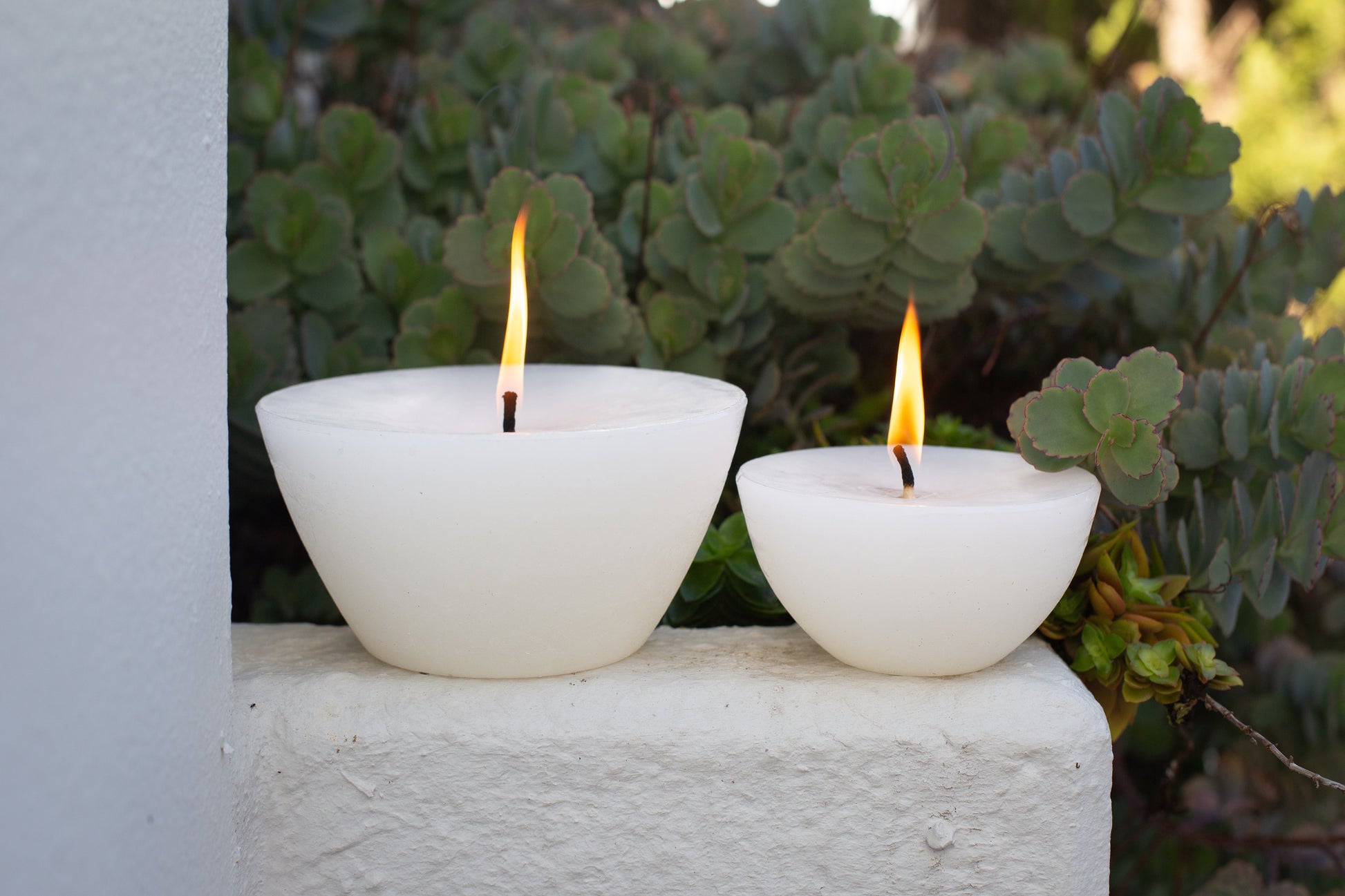 The two Luma Afrika Outdoor Bowls sitting on a ledge outside to show the difference scale. Infused with citronella & lavender to repell insects. 