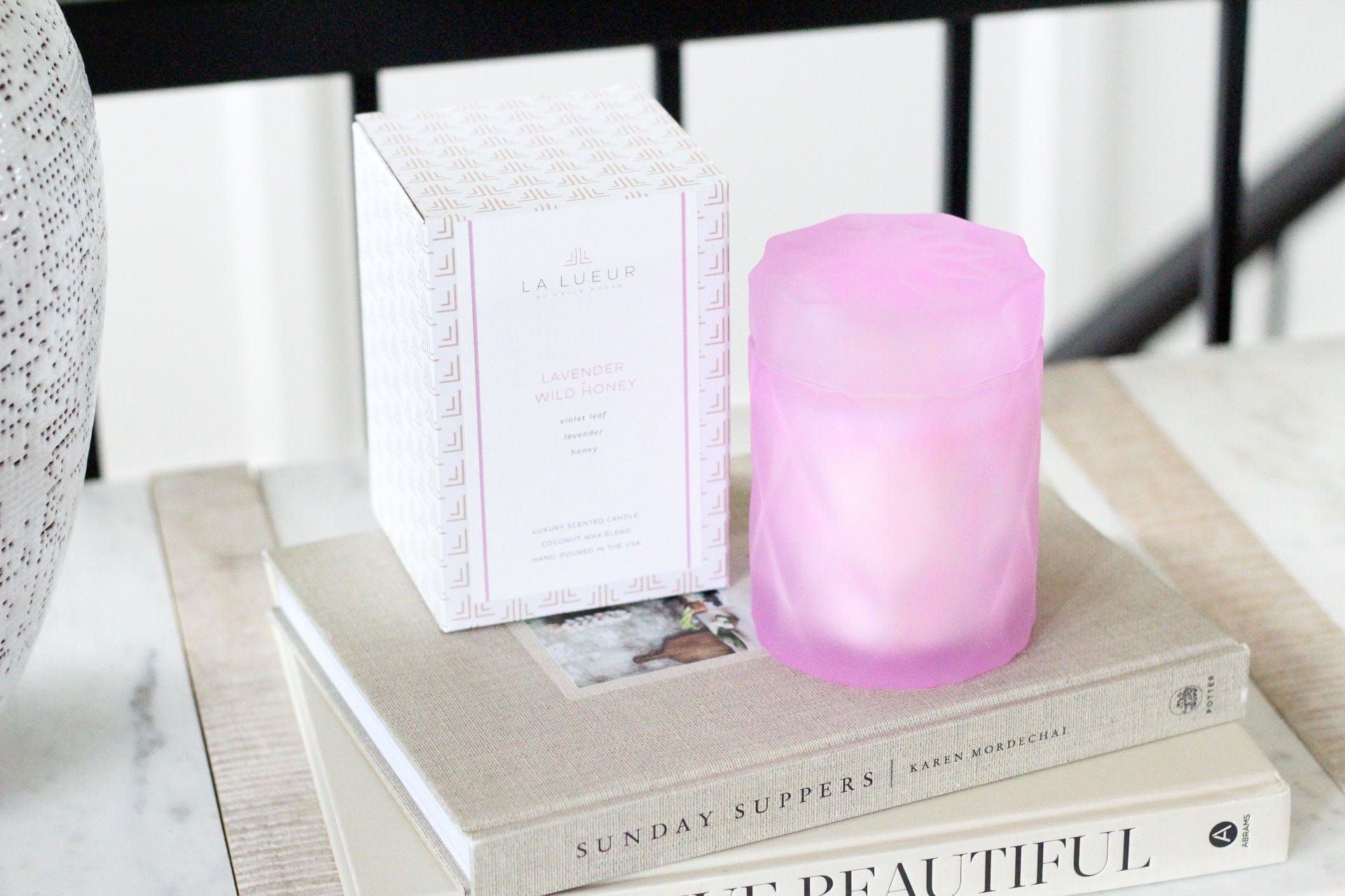 lavender lilac color glass candle jar with lid next to candle packaging box on stack of books