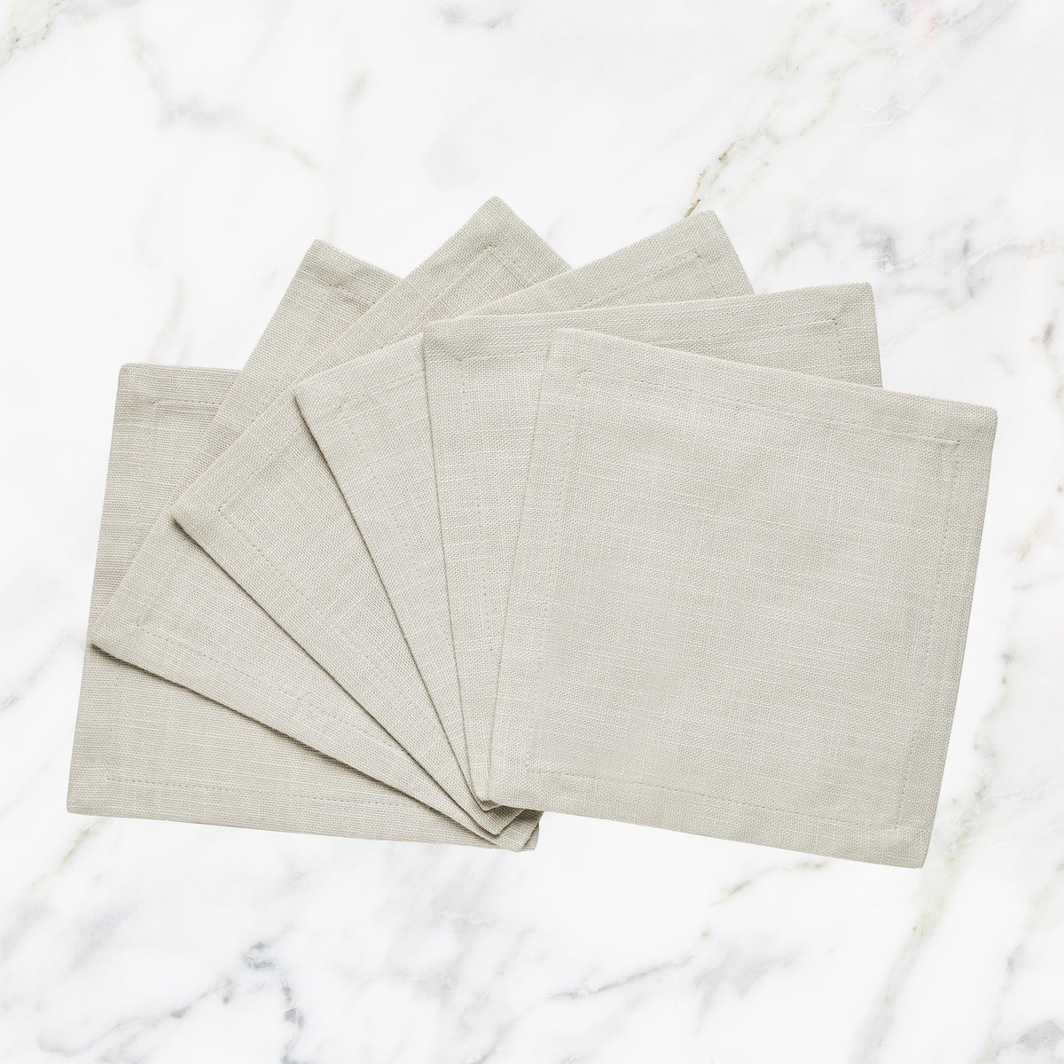 CNP-4912-66_1|Set of fan-folded natural beige linen dinner napkins on marble, ideal for elegant and reusable neutral table settings.