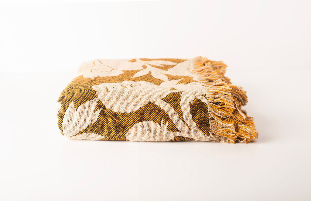 Front view of folded ochre gold and cream floral woven cotton throw on a white background