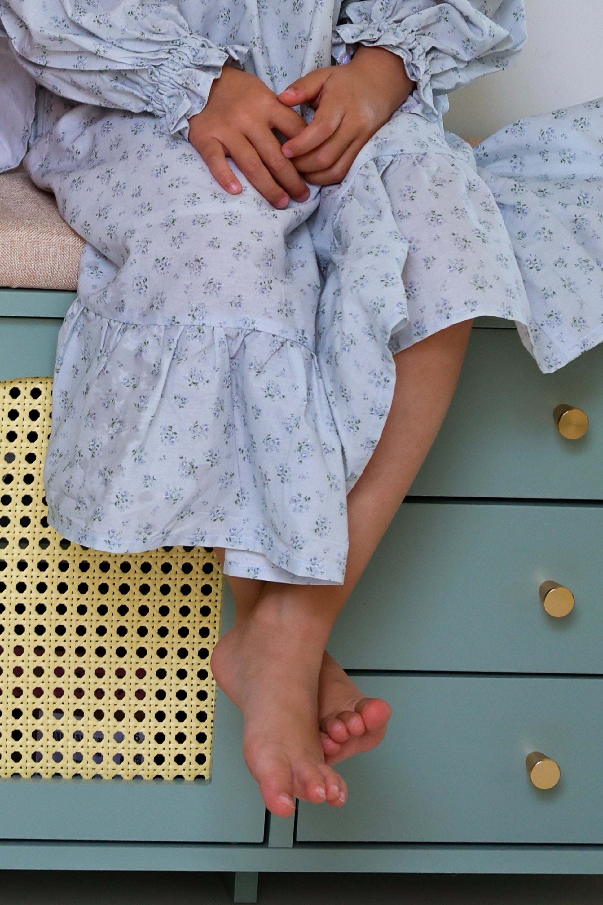 Person wearing a light blue floral dress sitting on a green dresser.