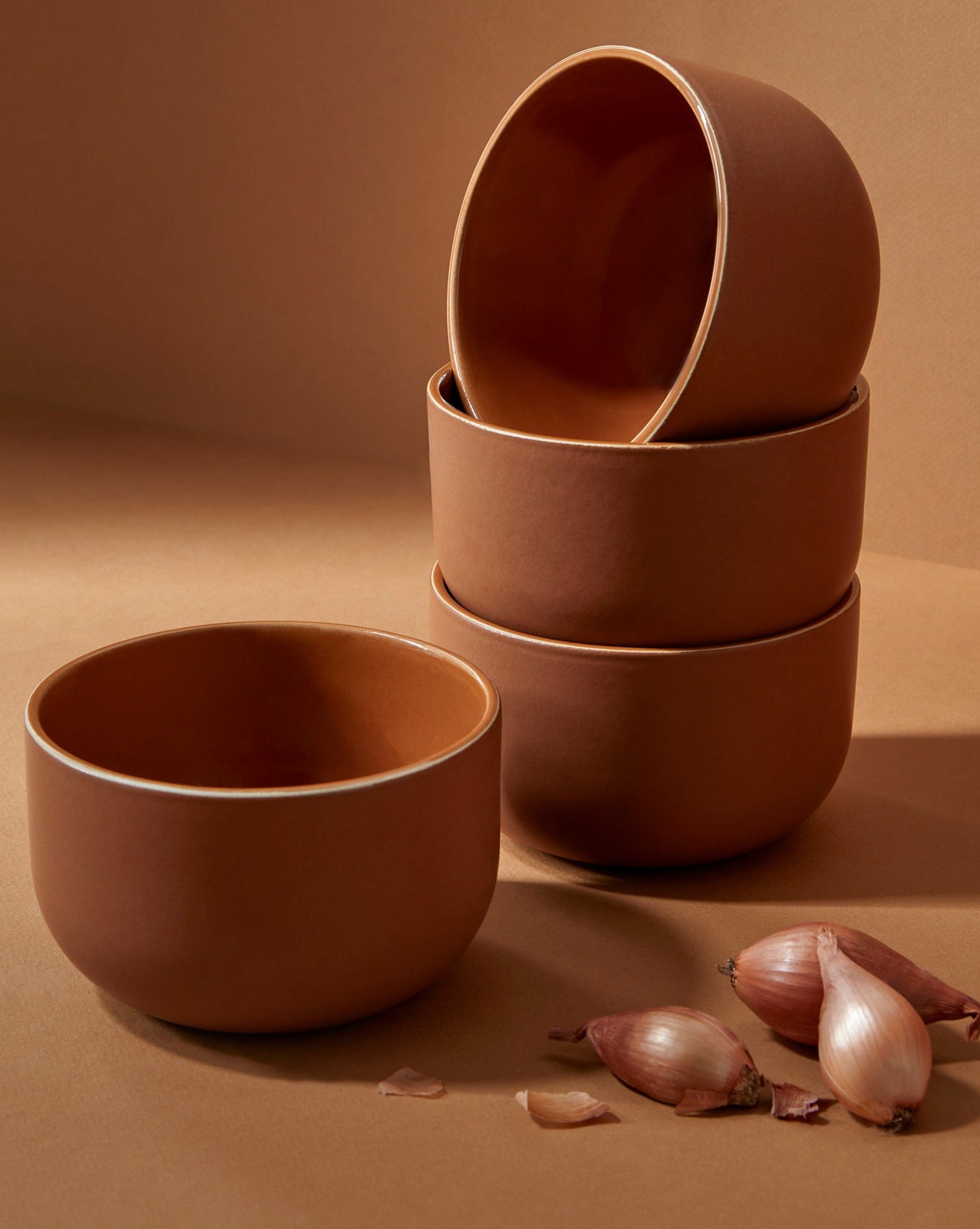 A set of beige stoneware dinnerware including flat dinner plates, flat salad plates, pasta plates/bowls, and dinner bowls, displayed with garlic and nuts on the plates.