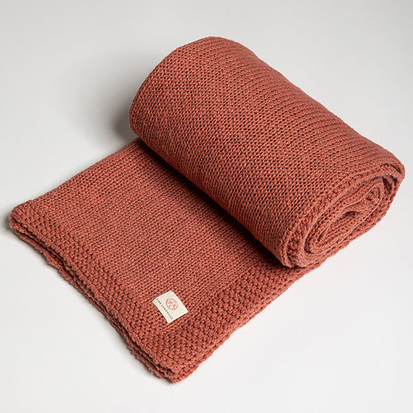 Rolled-up organic cotton rosewood pink blanket with a Pink Lemonade label on a light gray background.